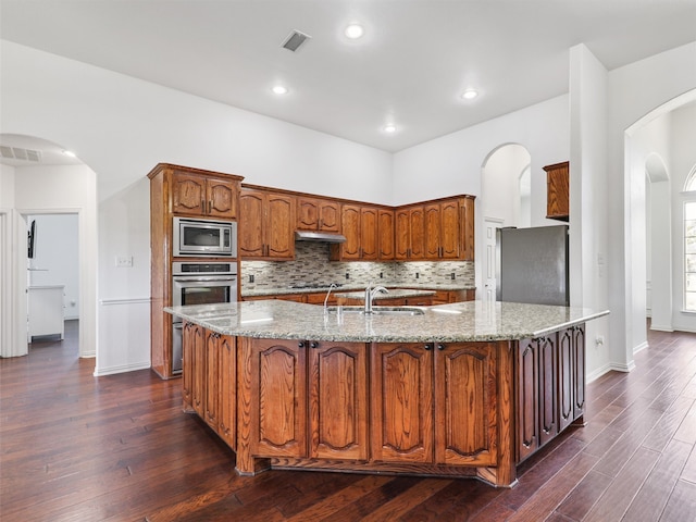 kitchen featuring light stone countertops, stainless steel appliances, dark hardwood / wood-style floors, and a kitchen island with sink