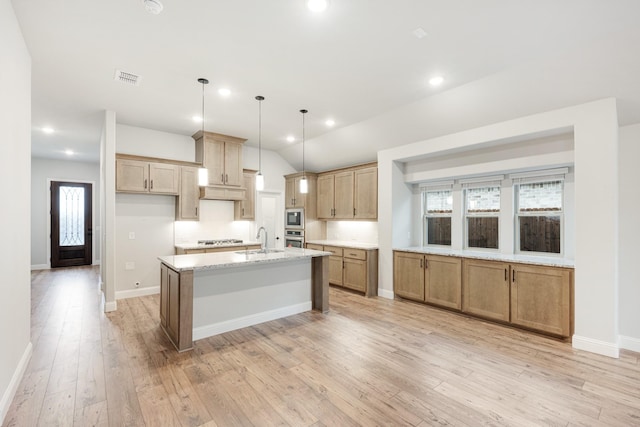 kitchen featuring sink, light wood-type flooring, a kitchen island with sink, and hanging light fixtures