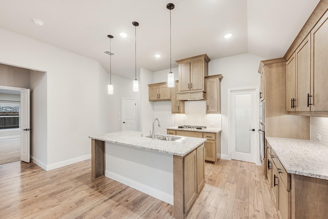 kitchen with sink, hanging light fixtures, light stone counters, an island with sink, and light wood-type flooring