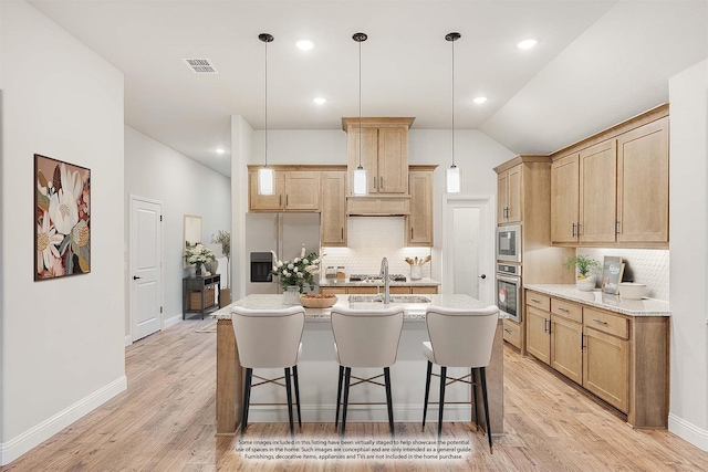 kitchen with pendant lighting, lofted ceiling, a kitchen island with sink, decorative backsplash, and appliances with stainless steel finishes