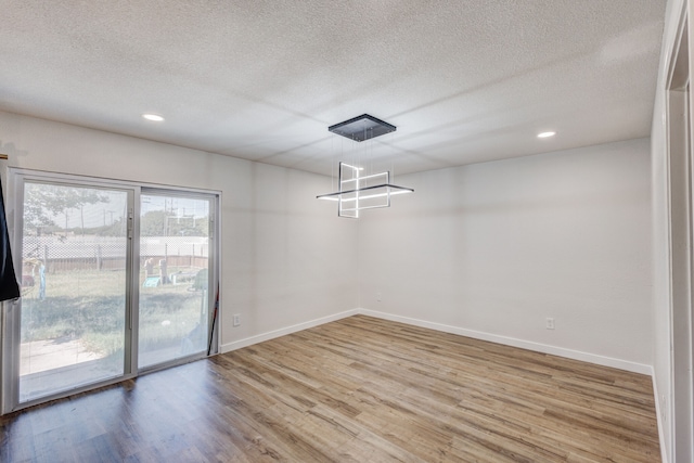 unfurnished dining area featuring wood-type flooring, a notable chandelier, and a textured ceiling