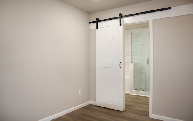 unfurnished bedroom with a barn door, ensuite bath, and dark hardwood / wood-style flooring