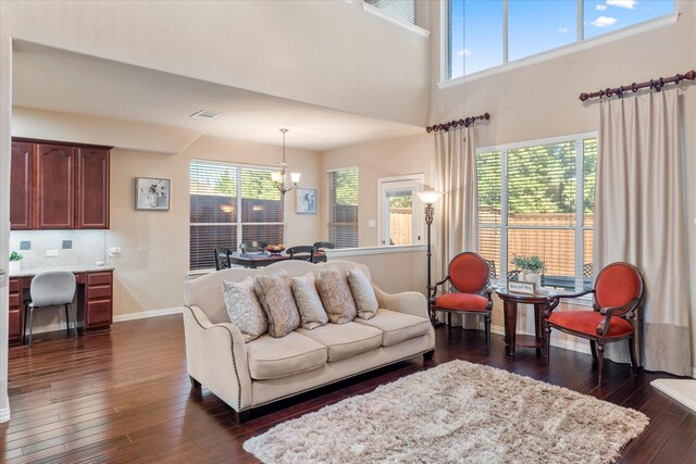 living room featuring dark hardwood / wood-style floors, a healthy amount of sunlight, a towering ceiling, and an inviting chandelier