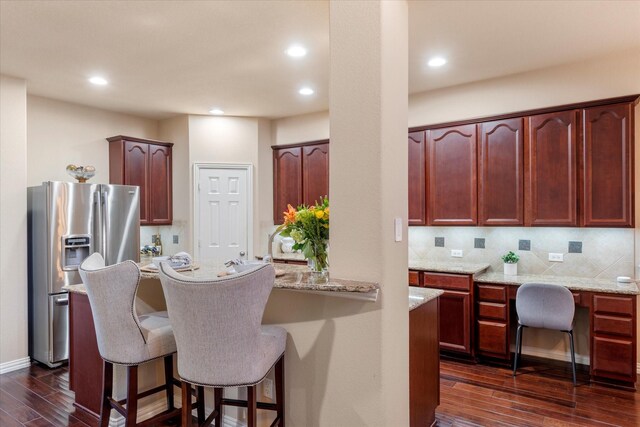 kitchen with dark wood-type flooring, a kitchen breakfast bar, stainless steel refrigerator with ice dispenser, tasteful backsplash, and light stone counters