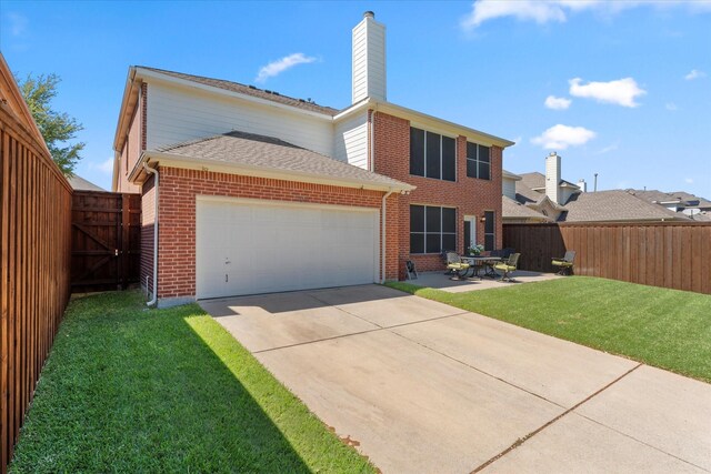 rear view of property featuring a lawn, a patio area, and a garage