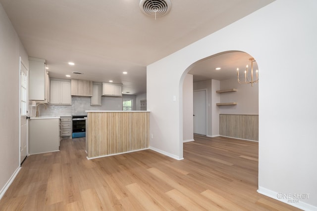 kitchen featuring light hardwood / wood-style floors, sink, stainless steel range with electric cooktop, white cabinetry, and an inviting chandelier