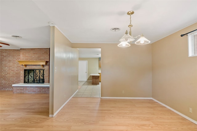 empty room featuring light hardwood / wood-style flooring, ceiling fan with notable chandelier, and a fireplace