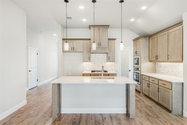 kitchen with hanging light fixtures, an island with sink, backsplash, appliances with stainless steel finishes, and sink