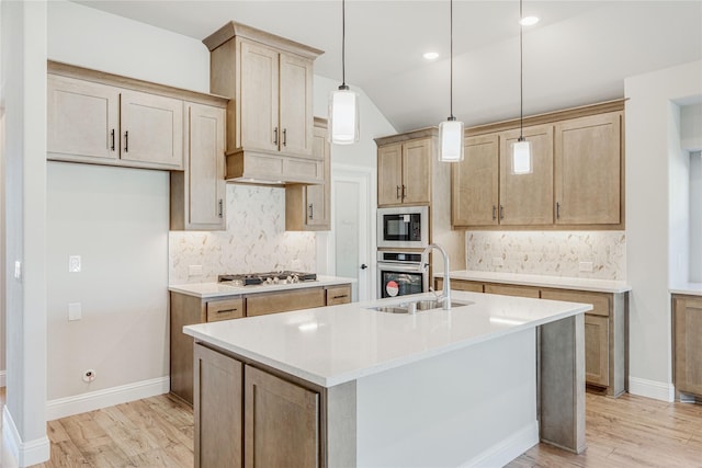 kitchen with sink, a kitchen island with sink, stainless steel appliances, decorative light fixtures, and light wood-type flooring