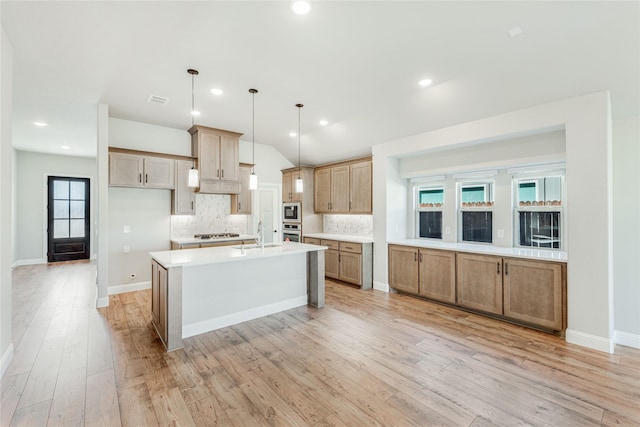 kitchen with vaulted ceiling, pendant lighting, backsplash, a center island with sink, and light wood-type flooring