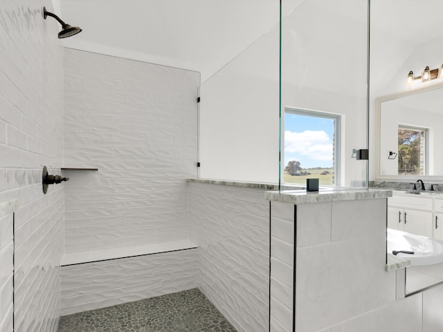 bathroom featuring lofted ceiling, sink, tile walls, and tiled shower