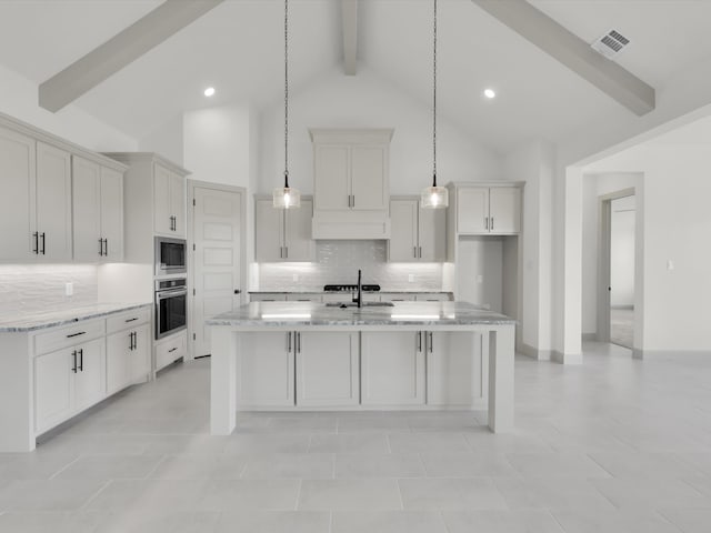 kitchen featuring beam ceiling, light stone countertops, an island with sink, decorative backsplash, and appliances with stainless steel finishes