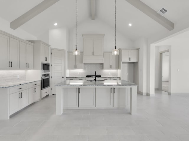 kitchen with hanging light fixtures, light stone counters, stainless steel appliances, a center island with sink, and beam ceiling