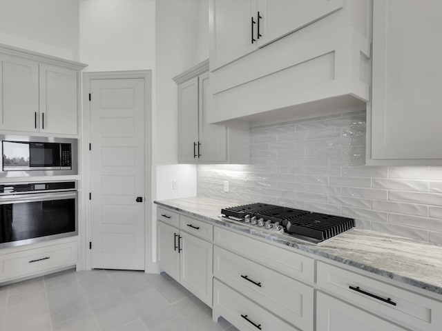 kitchen with white cabinets, decorative backsplash, light stone countertops, appliances with stainless steel finishes, and light tile patterned flooring