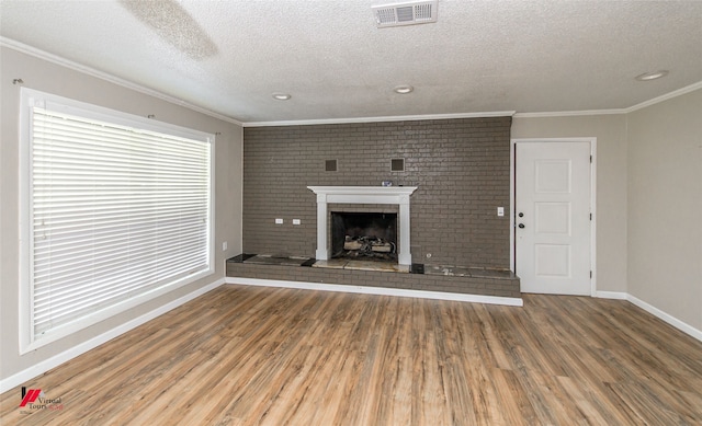 unfurnished living room featuring a textured ceiling, wood-type flooring, ornamental molding, and a brick fireplace