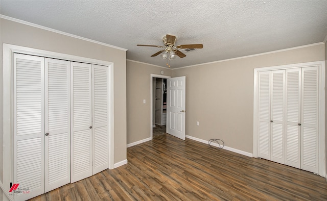 unfurnished bedroom featuring a textured ceiling, dark hardwood / wood-style floors, multiple closets, ornamental molding, and ceiling fan