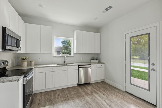 kitchen with stainless steel appliances, sink, light stone countertops, light hardwood / wood-style flooring, and white cabinets