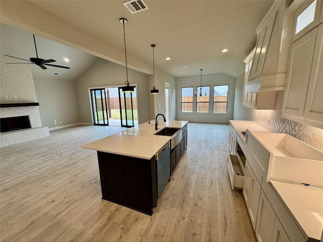 kitchen featuring ceiling fan, pendant lighting, light hardwood / wood-style flooring, a fireplace, and an island with sink