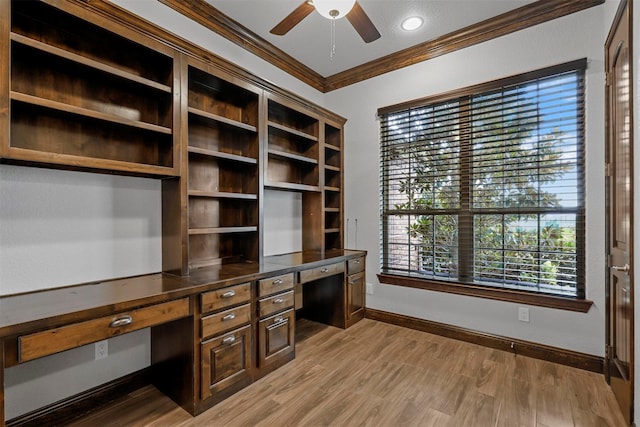 unfurnished office with ceiling fan, ornamental molding, built in desk, and light wood-type flooring