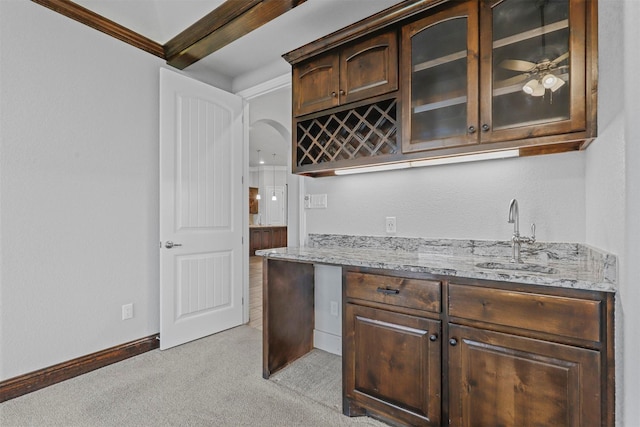 bar with sink, light stone counters, dark brown cabinetry, crown molding, and light carpet