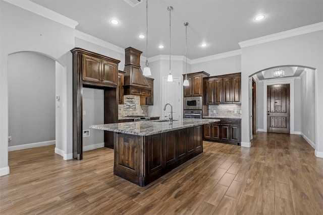 kitchen featuring light stone countertops, appliances with stainless steel finishes, dark brown cabinets, and a center island with sink