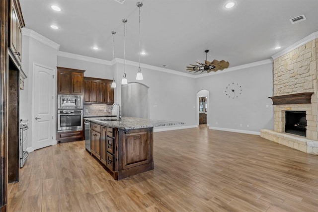 kitchen featuring sink, decorative light fixtures, dark brown cabinets, appliances with stainless steel finishes, and a kitchen island with sink