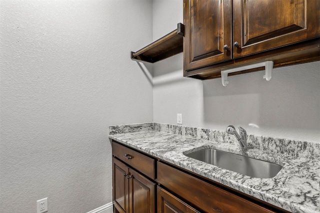 kitchen featuring light stone countertops, dark brown cabinets, and sink