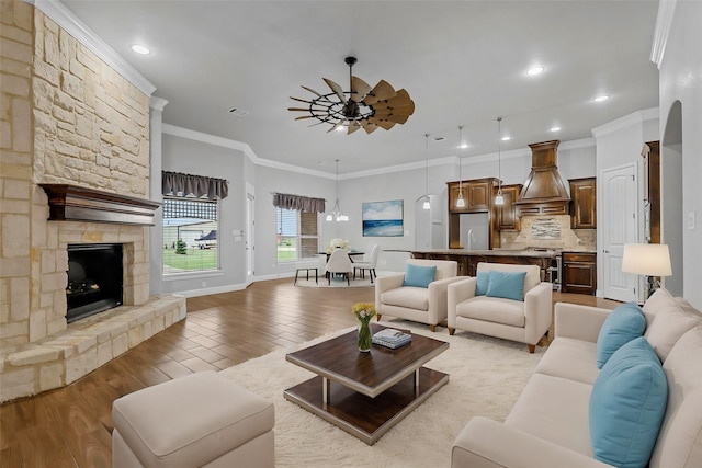 living room featuring a fireplace, crown molding, light hardwood / wood-style flooring, and ceiling fan