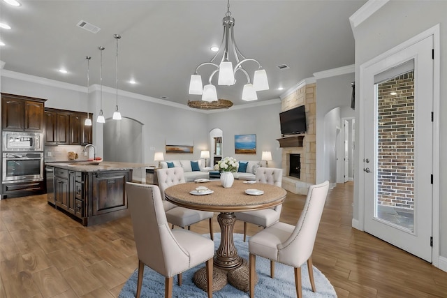 dining space with hardwood / wood-style flooring, crown molding, sink, and a fireplace