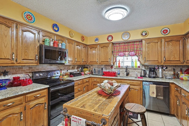 kitchen with light stone counters, light tile patterned flooring, sink, a textured ceiling, and black appliances