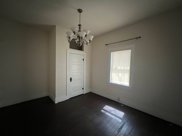 spare room with an inviting chandelier and dark hardwood / wood-style floors