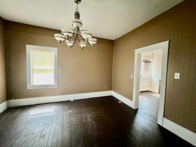 empty room featuring wooden walls, an inviting chandelier, and dark wood-type flooring