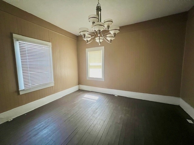 unfurnished room with an inviting chandelier, wood walls, and dark hardwood / wood-style flooring