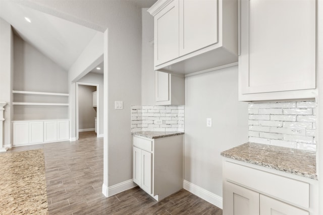 kitchen with decorative backsplash, white cabinetry, light stone counters, lofted ceiling, and hardwood / wood-style floors