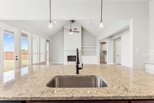 kitchen with light stone counters, ceiling fan, hanging light fixtures, and sink