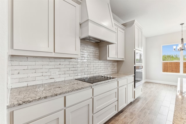 kitchen featuring premium range hood, decorative light fixtures, white cabinetry, stainless steel appliances, and an inviting chandelier