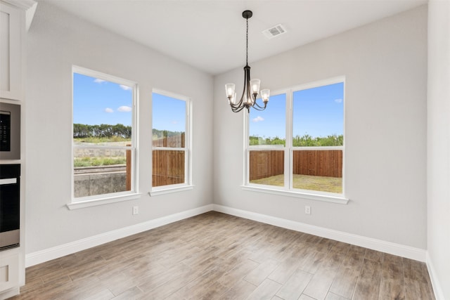 unfurnished dining area featuring an inviting chandelier and hardwood / wood-style flooring