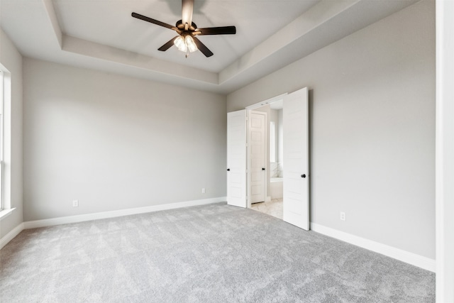 unfurnished bedroom with a tray ceiling, ceiling fan, light colored carpet, and ensuite bath