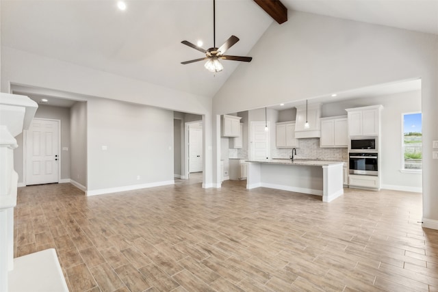 unfurnished living room featuring beamed ceiling, sink, light hardwood / wood-style flooring, high vaulted ceiling, and ceiling fan