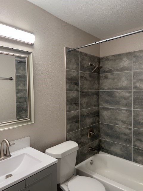 full bathroom featuring tiled shower / bath, vanity, toilet, and a textured ceiling