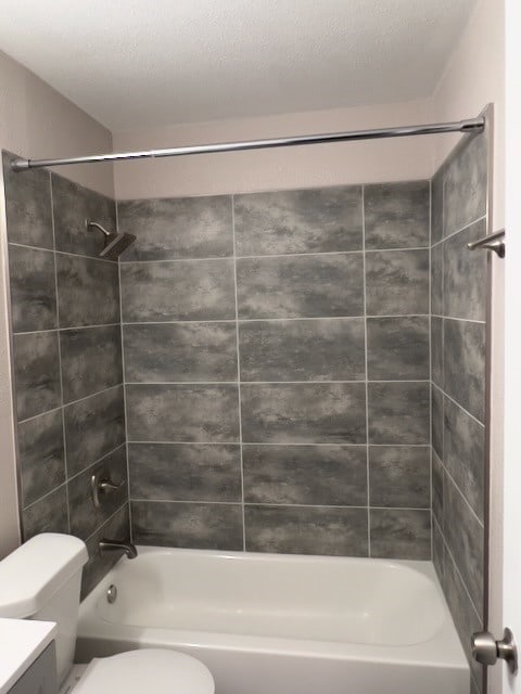 full bathroom featuring tiled shower / bath, vanity, toilet, and a textured ceiling