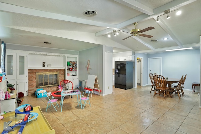 interior space featuring lofted ceiling with beams, a brick fireplace, ceiling fan, and light tile patterned floors