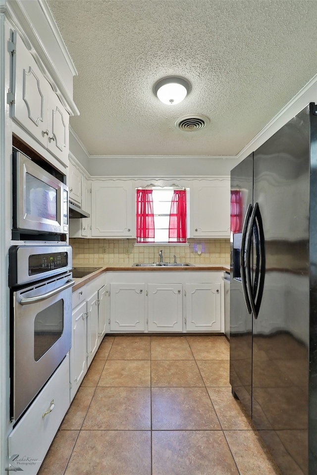 kitchen with sink, light tile patterned floors, white cabinetry, stainless steel appliances, and decorative backsplash