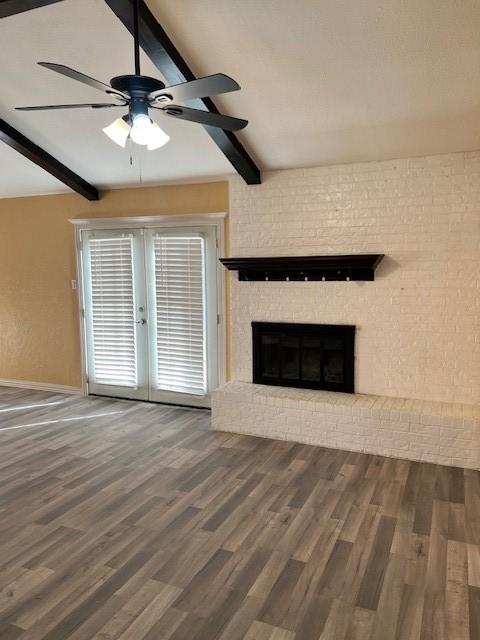 unfurnished living room with lofted ceiling with beams, dark hardwood / wood-style flooring, ceiling fan, a brick fireplace, and french doors