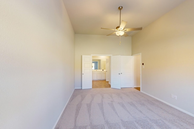 unfurnished bedroom featuring ceiling fan, light colored carpet, a towering ceiling, and ensuite bath