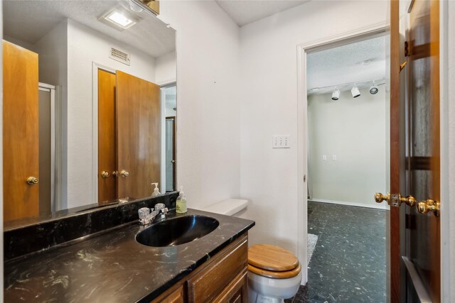 bathroom featuring vanity, toilet, a shower with door, and a textured ceiling