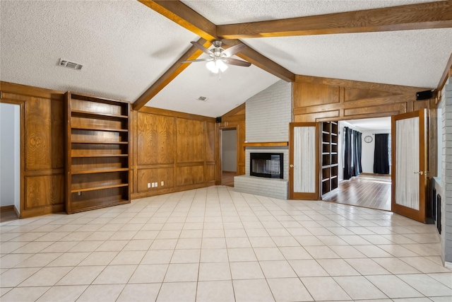 unfurnished living room featuring wood walls, lofted ceiling with beams, ceiling fan, a textured ceiling, and a fireplace