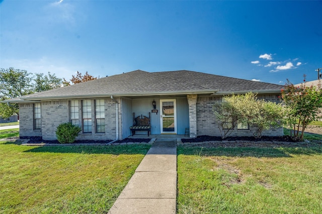 view of front of home featuring brick siding, roof with shingles, and a front yard