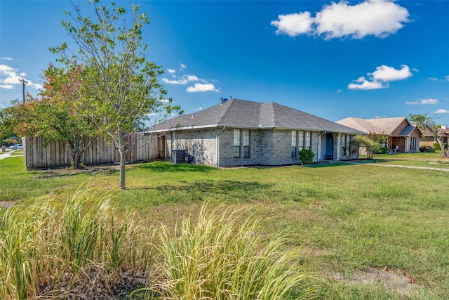 view of side of property with fence, roof with shingles, central air condition unit, a lawn, and brick siding