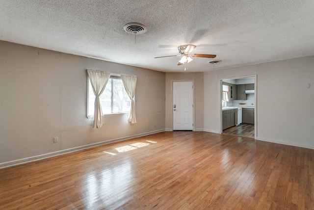 empty room with a textured ceiling, ceiling fan, and light hardwood / wood-style floors